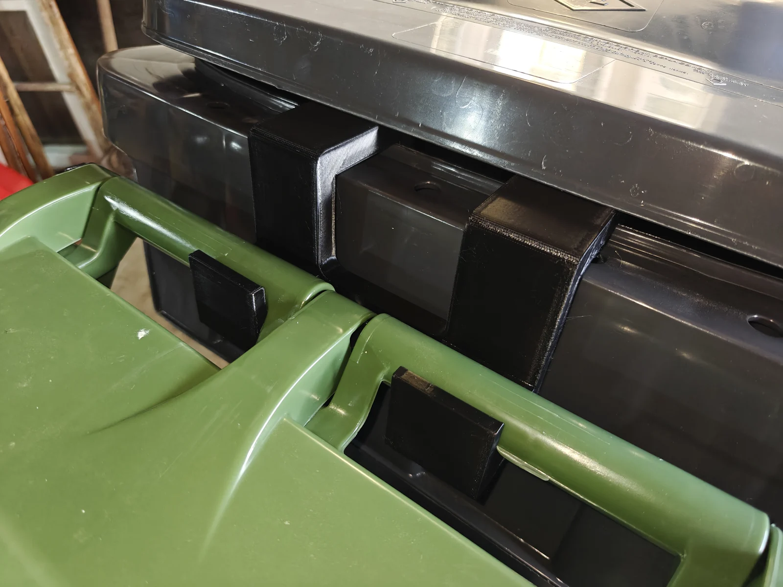 Black BinBuddy hanger over the grey rim, holding the green bin's rear handle